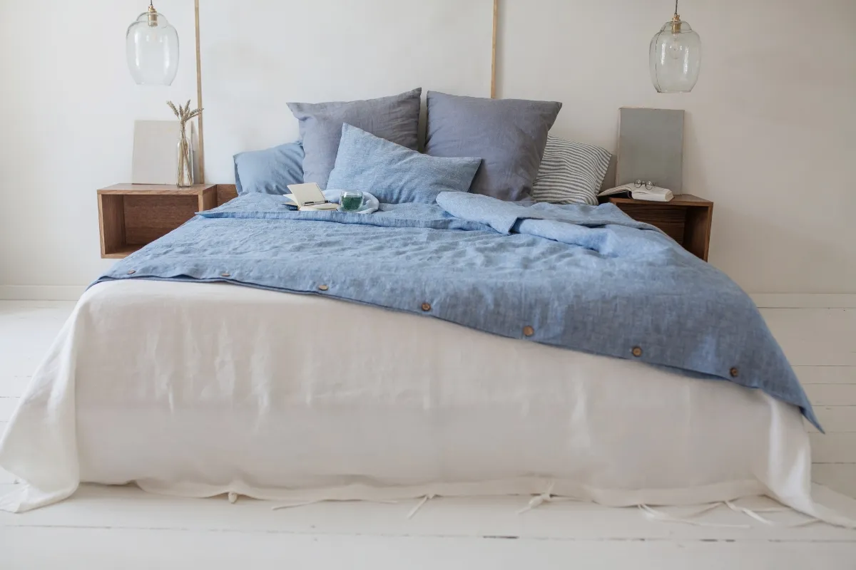 Soft blue and white washed linen duvet cover set on a bed with large grey pillows and natural wood nightstands
